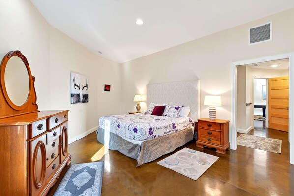 Un dormitorio con cama, cómoda, mesitas de noche y una puerta que da a otra habitación.