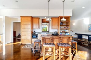 A kitchen with wooden cabinets, a central island with stools, pendant lighting, and a microwave.