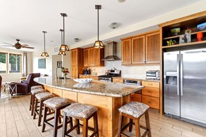 Una cocina moderna con una isla central, taburetes de bar, armarios de madera y electrodomésticos de acero inoxidable.