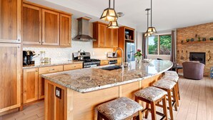 Una cocina moderna con armarios de madera, una isla grande con taburetes de bar, iluminación colgante y una pared de ladrillo.