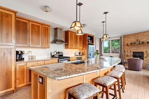 A modern kitchen with wooden cabinets, a large island with bar stools, pendant lighting, and a brick wall.