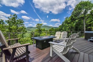 Um deck com cadeiras Adirondack, um braseiro e vista para uma cadeia montanhosa arborizada.