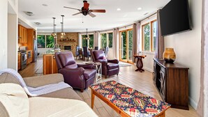 Amplia sala de estar con chimenea, sofás de cuero, televisor y cocina al fondo.