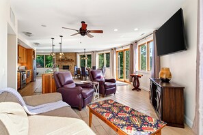 A spacious living area with a fireplace, leather sofas, a television, and a kitchen in the background.