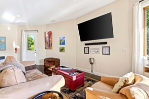 A living room with a flat-screen TV mounted on the wall, a door leading outside, and a window with curtains.