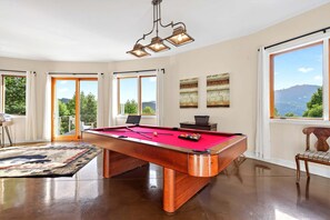 A pool table with a red felt surface, a wooden frame, and a hanging light fixture above it.