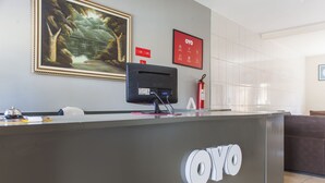 A reception desk with a monitor, framed artwork, and a fire extinguisher. - OYO M&J Hotel (Santo Antônio do Descoberto)