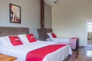 A hotel room with two beds, a chair, a table, and a painting on the wall.