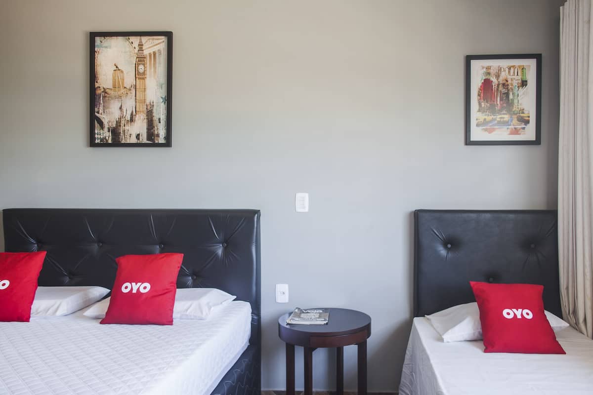 Two beds with black headboards, white bedding, and red pillows with 'OYO' branding.