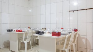 A kitchen with white tiled walls, a white countertop, and white chairs. There are various kitchen items on the counter, including a red basket, a black basket, and a white bowl. - OYO M&J Hotel (Santo Antônio do Descoberto)