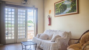A living room with a white couch, a wicker chair, a small table, and a painting on the wall. - OYO M&J Hotel (Santo Antônio do Descoberto)