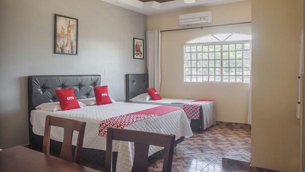 A hotel room with two beds, a dining table, and a window with a view. - OYO M&J Hotel (Santo Antônio do Descoberto)