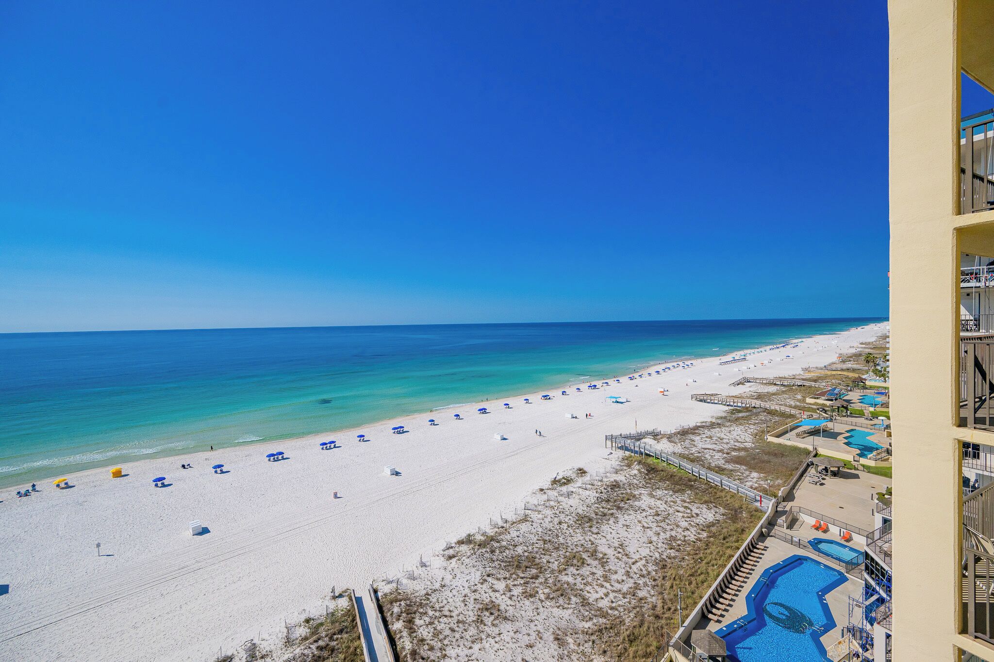 A beach with white sand, clear blue water, and a pool area with blue water.