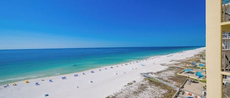 A beach with white sand, clear blue water, and a pool area with blue water.