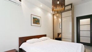 A bedroom with a wooden bed, white bedding, a framed picture on the wall, and a modern pendant light. - MinskLux Apartment 2 bedroom Nezavisimosti 12 (Minsk)