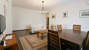 A living room with a dining table, chairs, a sofa, a coffee table, a TV, and a chandelier. - MinskLux Apartment 2 bedroom Nezavisimosti 12 (Minsk)
