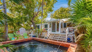 A backyard with a swimming pool, green chairs, and a covered patio area.