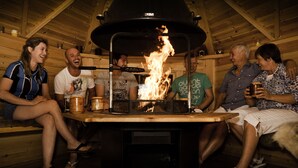 Un gruppo di persone sedute attorno a una stufa a legna in una rustica baita di legno con tetto spiovente.