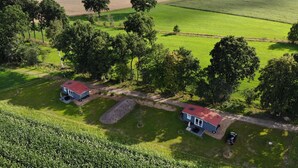Paesaggio rurale con due piccole case, un ampio campo aperto e turbine eoliche in lontananza.