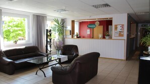 A reception area with a reception desk, two leather sofas, a glass coffee table, and a potted plant. - Schlafhaus Dünenweg 16 (Heringsdorf)