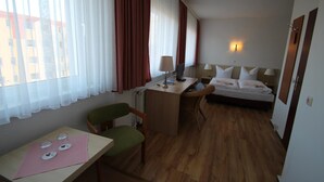 A hotel room with a bed, desk, chair, and a view of buildings through the window. - Schlafhaus Dünenweg 16 (Heringsdorf)