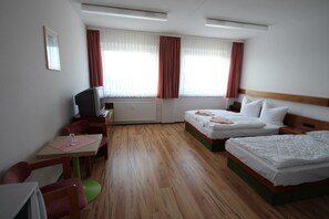 Une chambre d’hôtel avec deux lits, un bureau avec une chaise, une télévision et une fenêtre avec des rideaux.