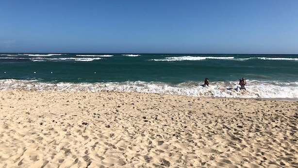 Ein sandiger Strand mit brechenden Wellen und blauem Himmel.