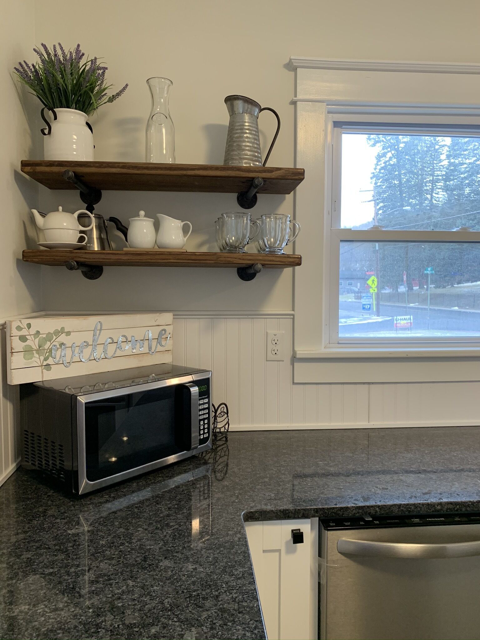A kitchen with a granite countertop, a stainless steel microwave, and a 'Welcome' sign.