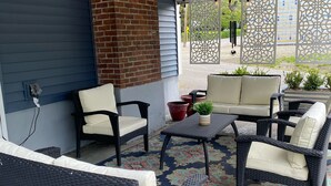 Ein überdachter Patio-Bereich mit Rattanmöbeln, einem gemusterten Teppich und einem Ziegelkamin.
