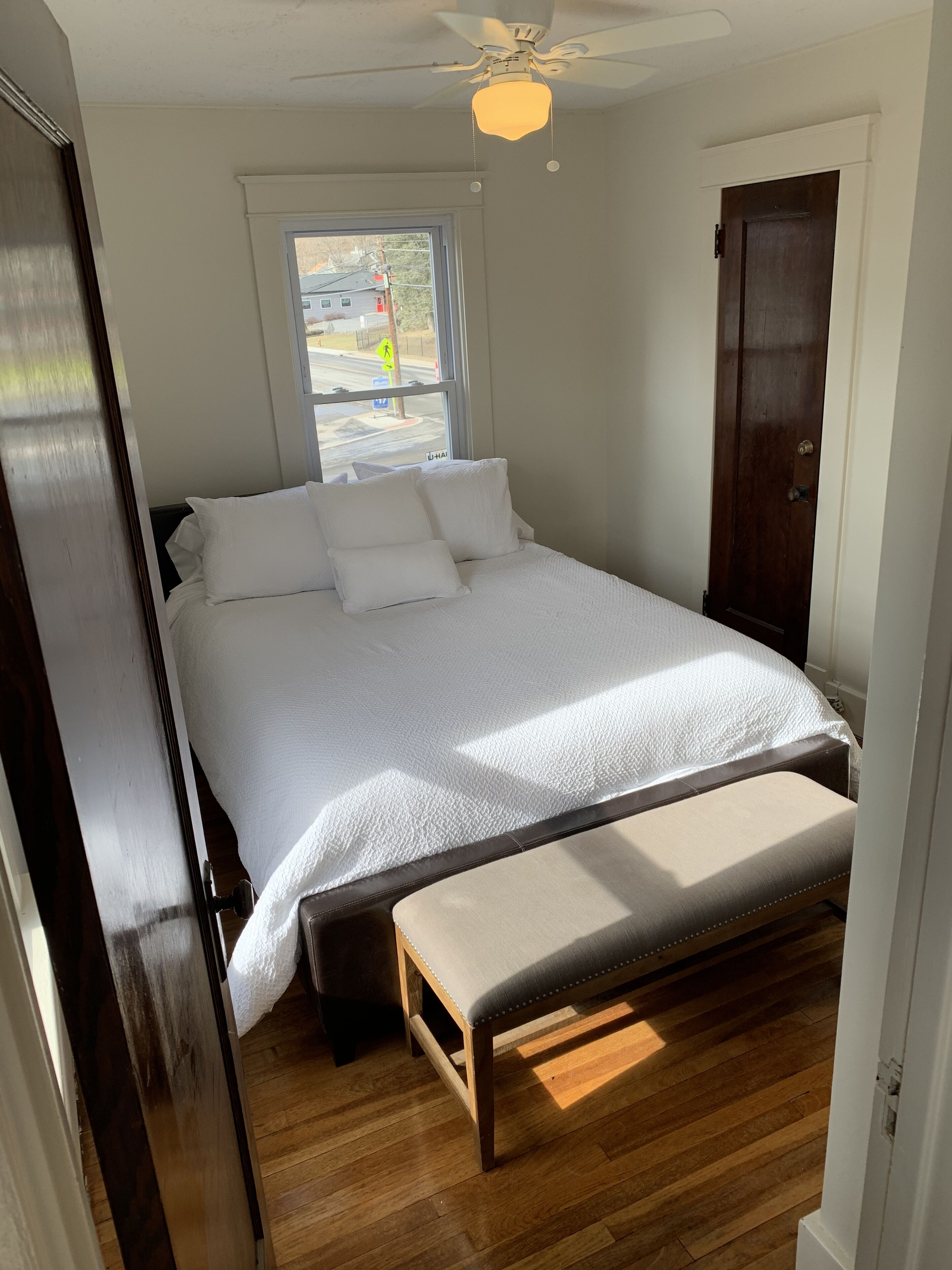 Una camera da letto con un letto, una panca, una ventola a soffitto, una finestra e una porta.