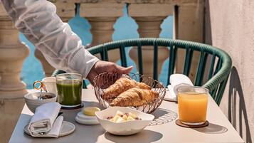 A table with breakfast items including croissants, a bowl of fruit, a glass of orange juice, and a green beverage.