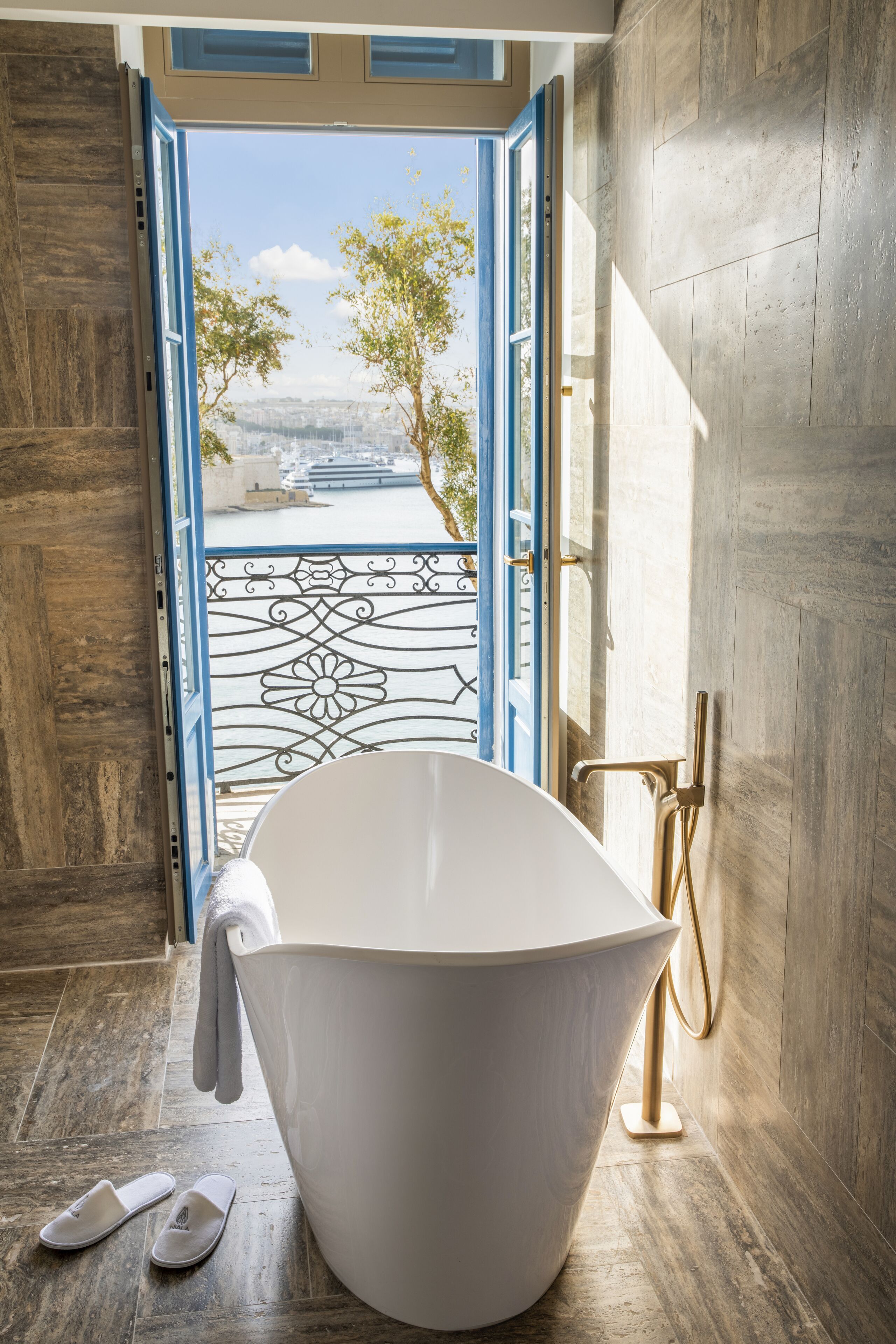 A modern bathroom with a freestanding bathtub, a view through an open door, and a pair of slippers on the floor.
