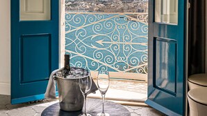 Un balcon donnant sur un paysage urbain, une table avec une bouteille et un verre à vin, et une porte bleue.