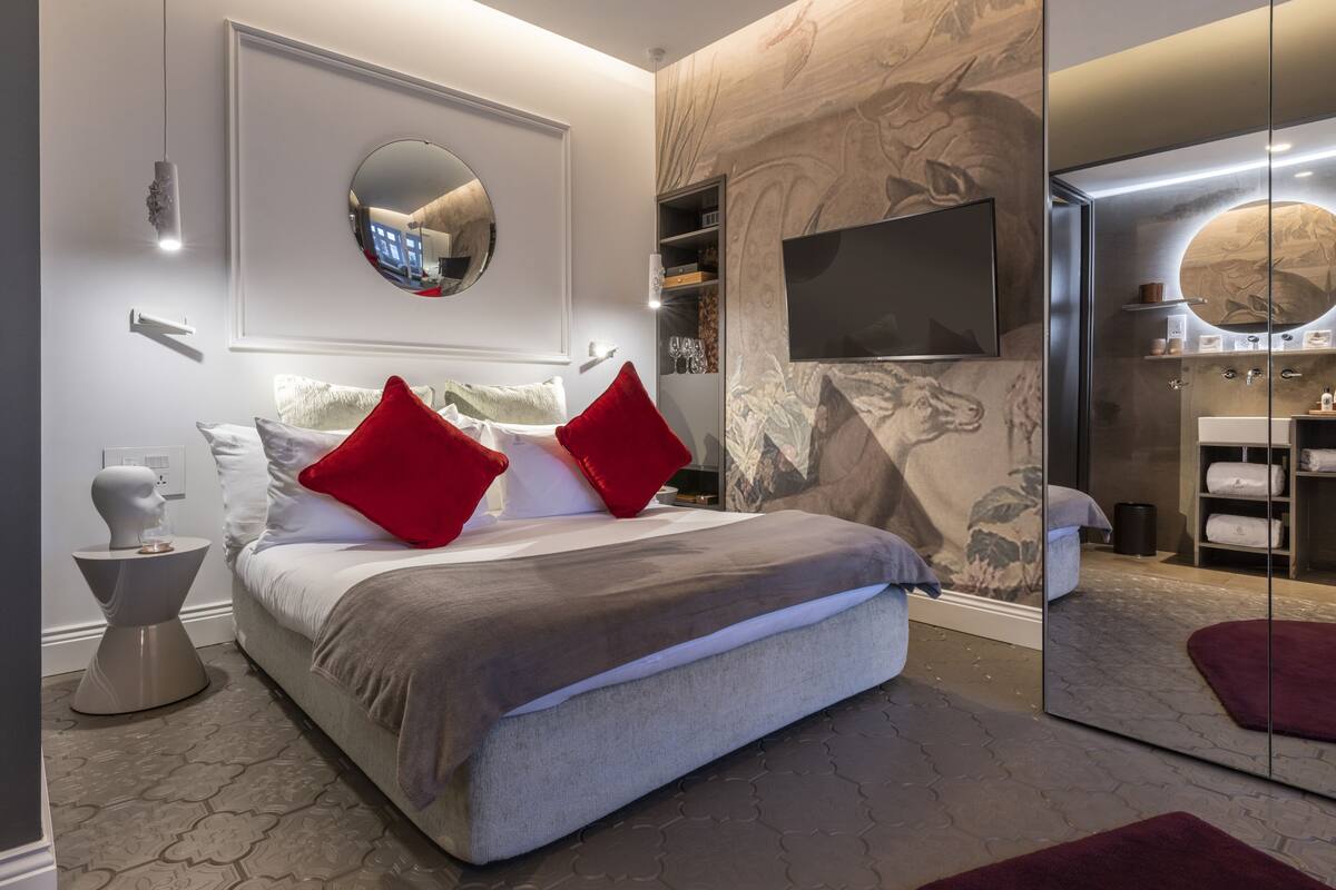 Un dormitorio moderno con una cama grande, un espejo redondo, un televisor y un baño con paredes de vidrio.