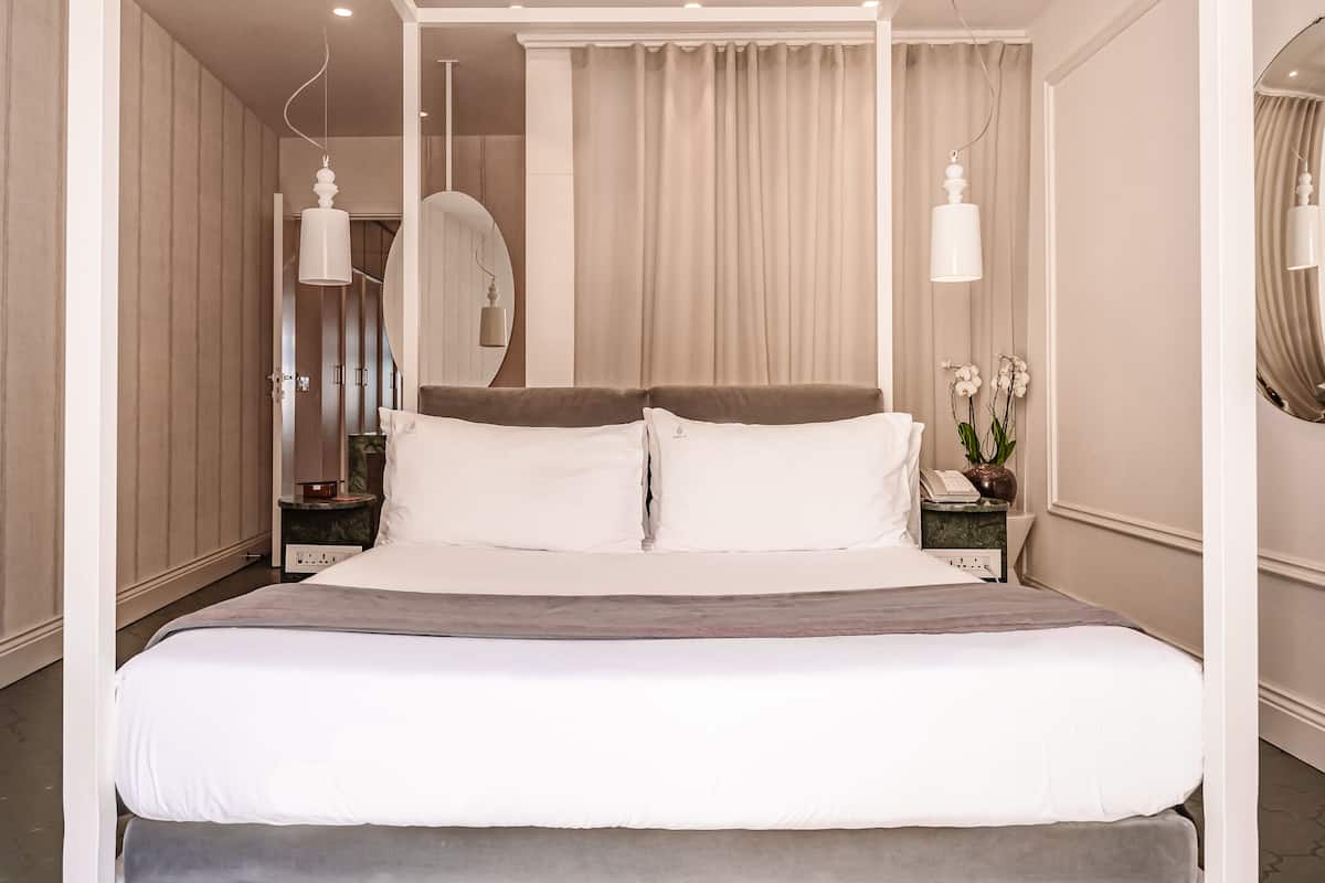 Una cama grande con sábanas blancas, una mesita de noche con una lámpara y un espejo en la pared.