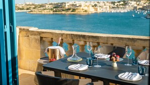 Une table dressée pour le dîner, avec vue sur la mer et des bâtiments en arrière-plan.