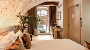 Une chambre avec un plafond en pierre, un grand lit, un bureau et une fenêtre avec des rideaux.
