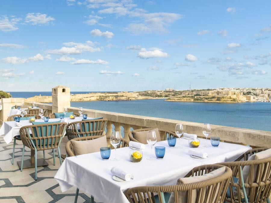 Ein Restaurant direkt am Meer mit gedeckten Tischen, mit Blick auf eine Küstenstadt und das Meer.