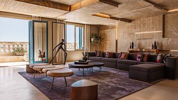 A modern living room with a large sofa, coffee table, and ottoman, a balcony with plants, and a view of the city.