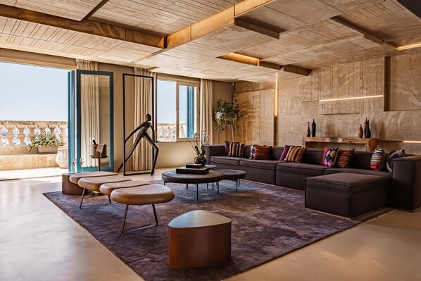 A modern living room with a large sofa, coffee table, and ottoman, a balcony with plants, and a view of the city.