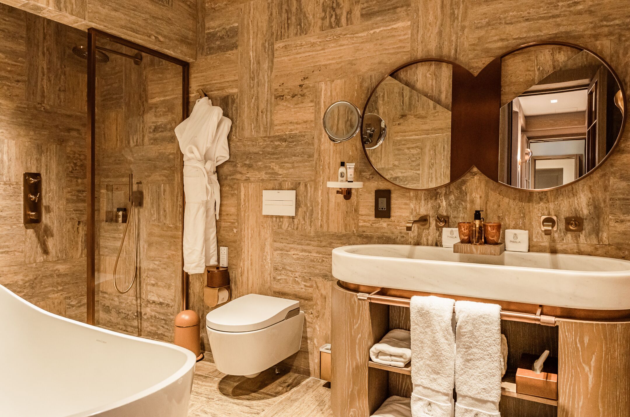 Un baño moderno con pared de madera, una bañera independiente, un inodoro y un tocador con un espejo grande.