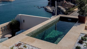 A rooftop pool with clear water, a view of the sea, and a cityscape in the background.