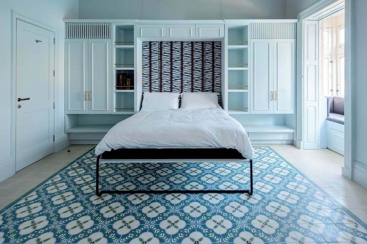 Un dormitorio con piso estampado, cama con ropa de cama blanca y armarios empotrados.