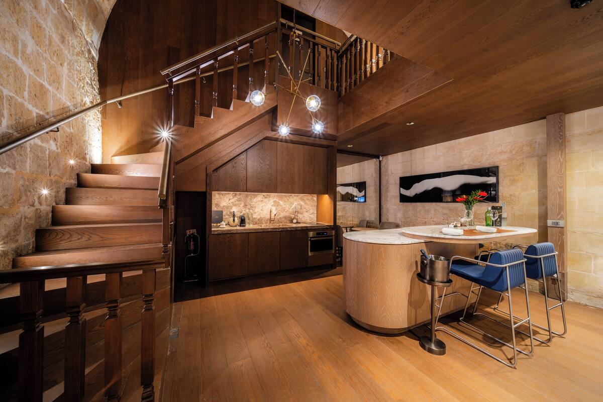 Una cocina moderna con una escalera de madera, una isla redonda y una pared de piedra.