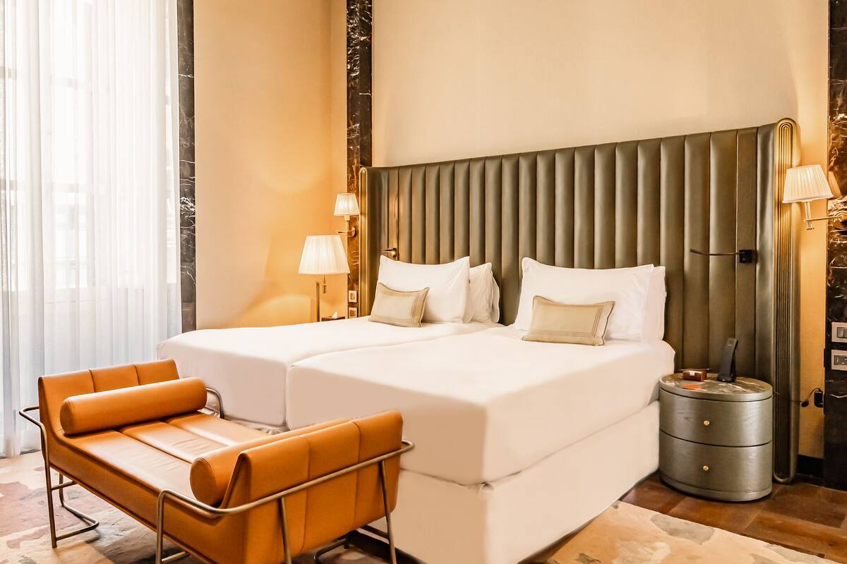Una habitación de hotel con una cama grande, dos mesitas de noche, una silla y una lámpara.