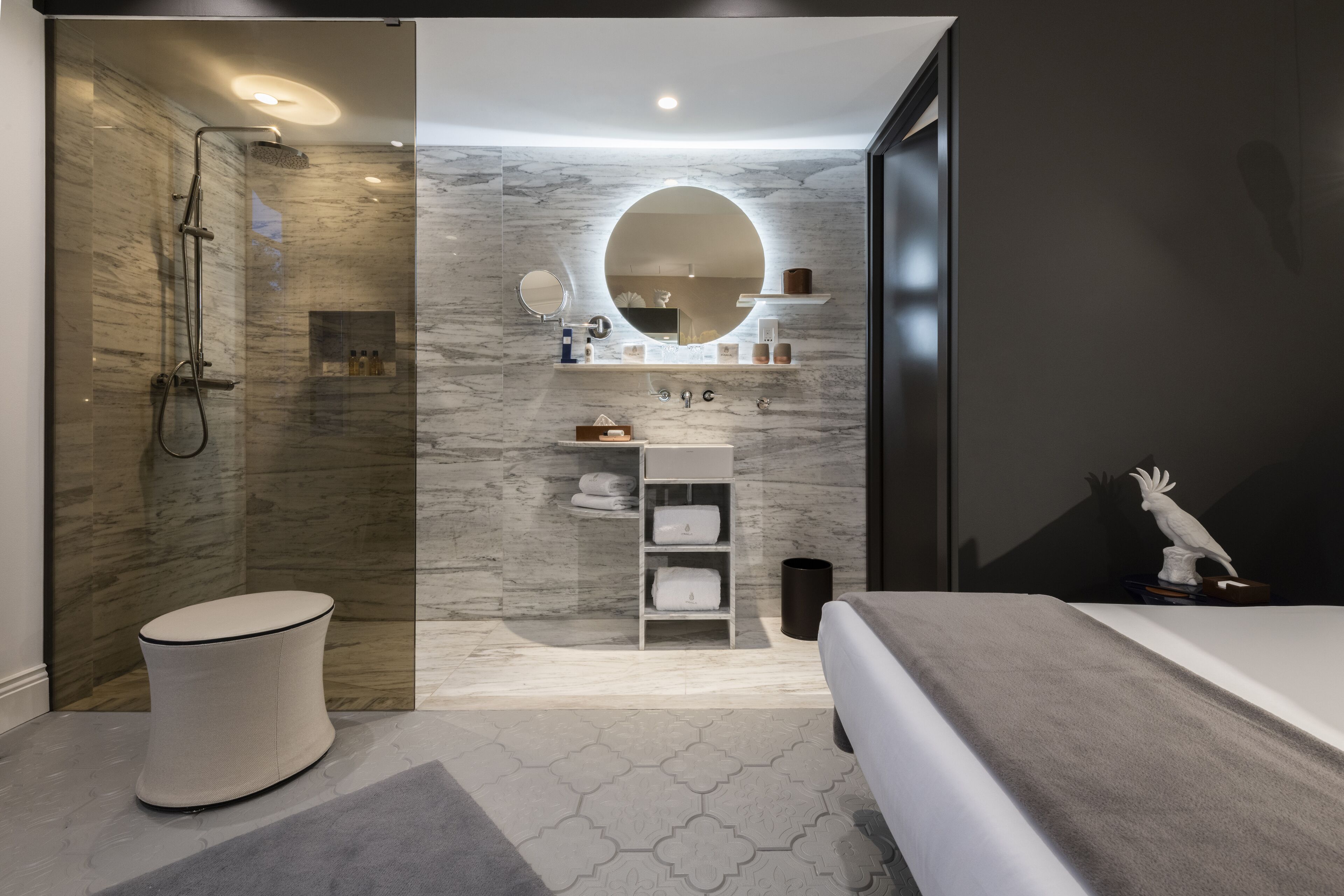 A modern bathroom with a glass-enclosed shower, a round mirror, and a built-in shelf with toiletries.