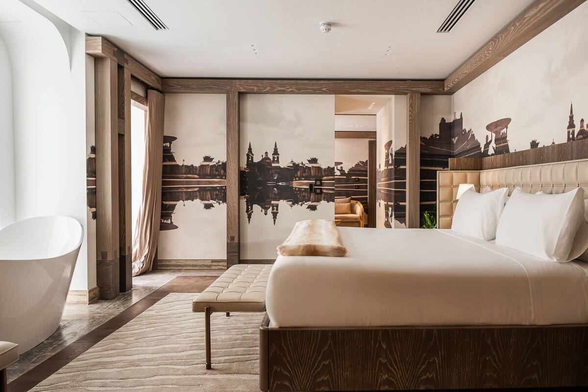 Una habitación de hotel moderna con una cama grande, un rincón de descanso y vistas a un mural urbano.