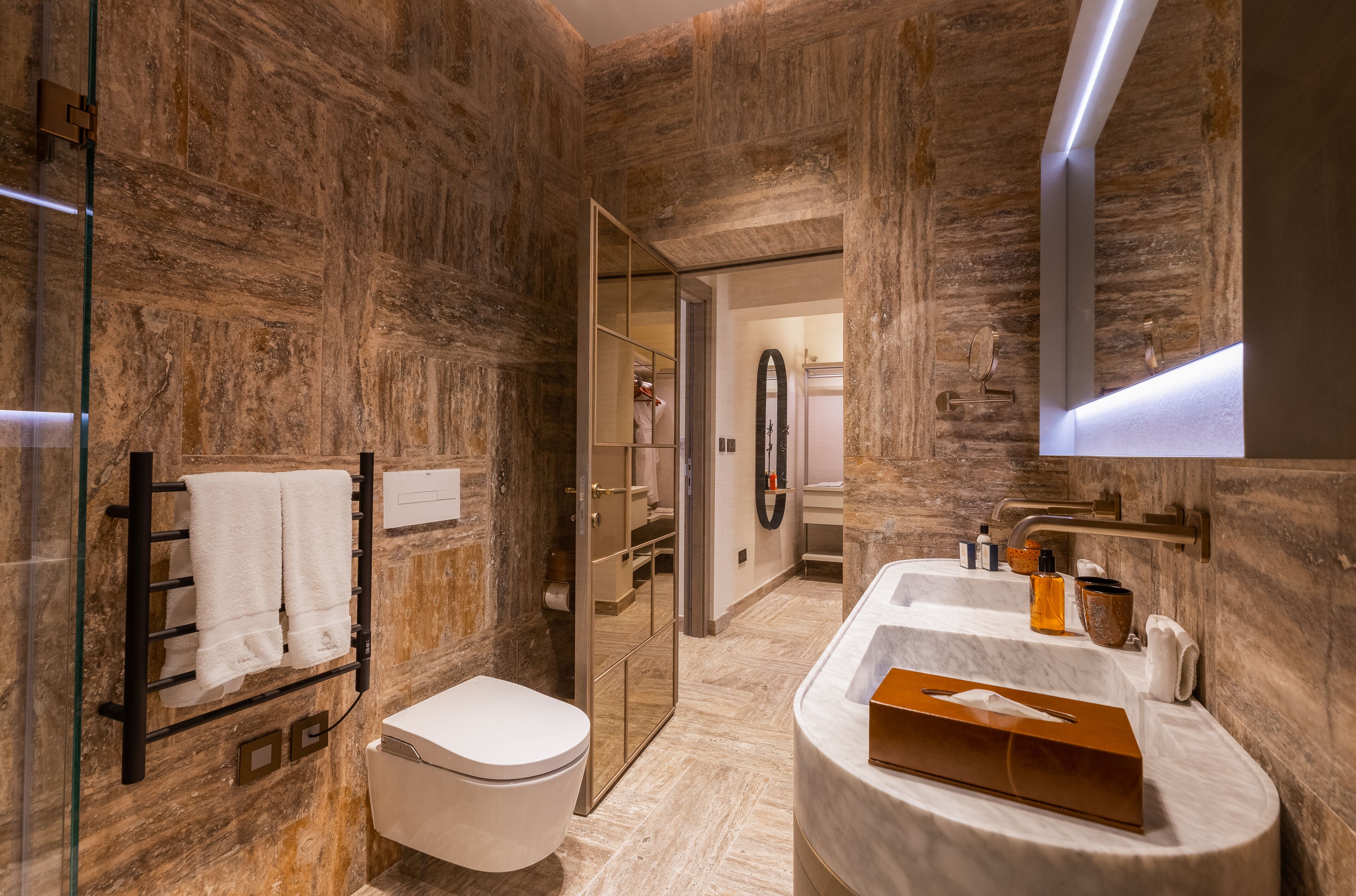 Ein modernes Badezimmer mit Marmorwand, einer Duschkabine aus Glas, einer weißen Toilette und einem Marmorwaschtisch mit Seifenspender.
