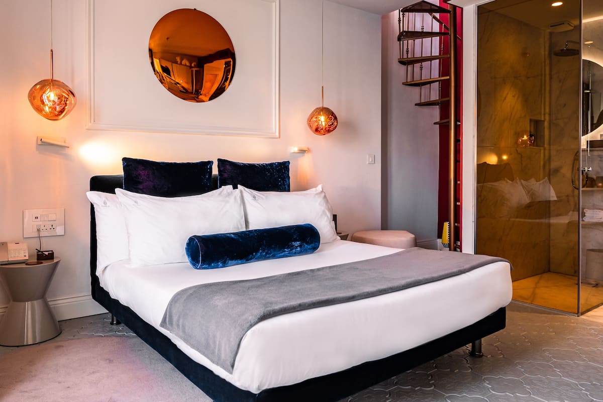 Un dormitorio moderno con una cama grande, lámparas de noche y una cabina de ducha de vidrio.