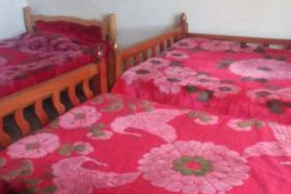 Une chambre avec deux lits en bois, chacun recouvert d’une courtepointe à motifs floraux rouges.